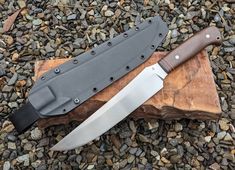 two knives sitting on top of a piece of wood next to rocks and gravel with stones in the background