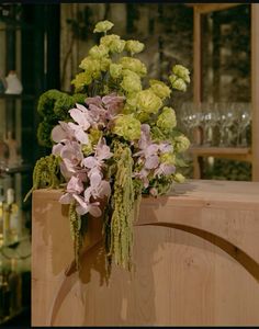 a vase filled with lots of flowers on top of a wooden table next to wine glasses