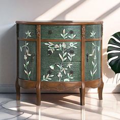 a green cabinet with flowers painted on it and a plant in the corner next to it