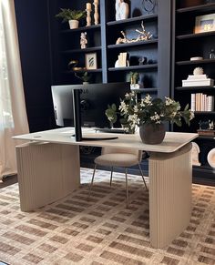 a desk with a computer on it in front of a book shelf filled with books