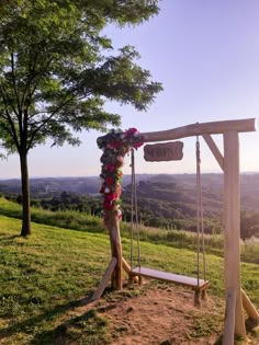 a wooden swing with flowers on it in the middle of a grassy area next to trees