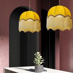 two yellow lamps hanging from the ceiling above a table with a potted plant on it