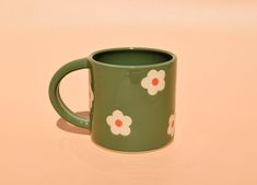 a green coffee mug with white and red flowers on it sitting on a pink surface