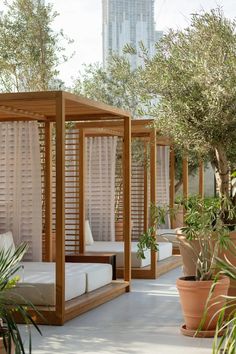 an outdoor bed with white sheets and pillows in the middle of a patio area surrounded by potted plants