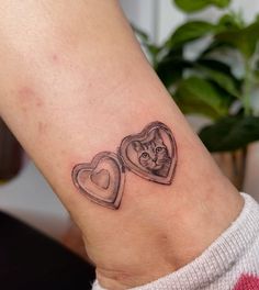 a cat in a heart shaped box tattoo on the ankle, with another cat behind it