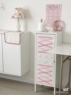 two white cabinets with pink ribbons on them in a girls's room, next to a desk and chair