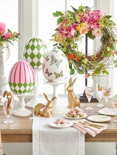 the table is set for easter dinner with flowers and eggs on it's pedestals