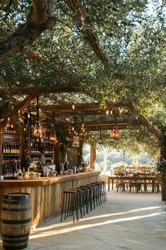 an outdoor bar with lots of chairs and lights hanging from the ceiling, surrounded by trees