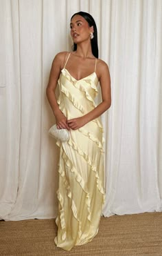 a woman standing in front of a white curtain wearing a yellow dress with ruffles