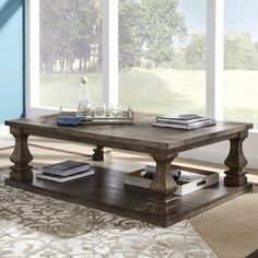 a coffee table with books on it in front of large windows and carpeted area