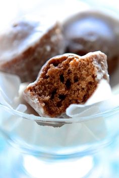 two chocolate donuts in a glass bowl with white frosting on the top and one half eaten