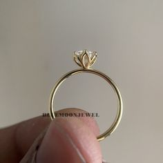 a close up of a person's hand holding a gold ring with a diamond