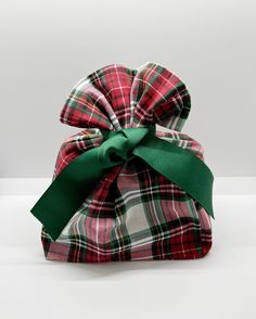 a red and green plaid gift bag tied with a green ribbon on a white surface