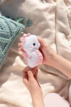 a person holding a small stuffed animal in their hand on a bed with blankets and pillows