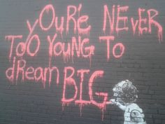 graffiti on the side of a brick building reads, you're never too young to dream big