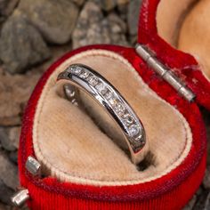 a diamond ring in a red velvet box on some rocks and stones with the lid open to show it's inside