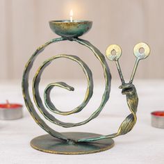 a metal candle holder with two candles in the shape of a snail on top of it