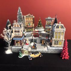 a toy town with cars and people on the street in front of buildings, trees, and snow