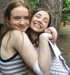 two girls hugging each other in front of a tree