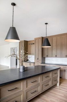 a large kitchen with wooden cabinets and black counter tops, two pendant lights over the island