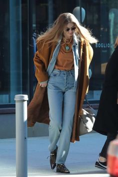 a woman walking down the street in jeans and an orange top with her hair blowing back