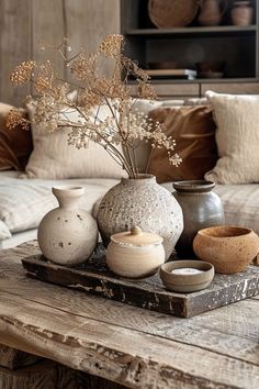 vases and bowls are sitting on a table in front of a couch with pillows