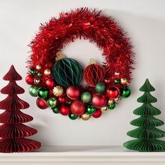 a christmas wreath with ornaments hanging on the wall next to two small green and red trees