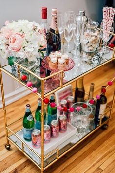 a gold bar cart filled with bottles and glasses on top of a hard wood floor