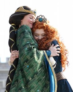 two women hug each other while dressed in costumes and accessories, one wearing a tiara