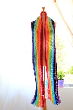 a multicolored scarf is hanging on a wooden stand in front of a window