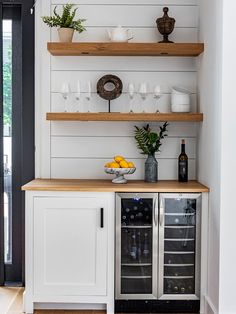 a white kitchen with open shelving and wine glasses on the counter top, next to a black door