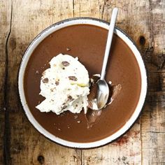 a bowl filled with chocolate pudding and ice cream on top of a wooden table next to a spoon