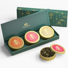 three tea tins in a green box with gold trimming and pink labels on them