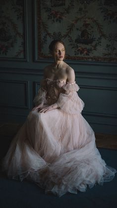 a woman in a pink dress is sitting on the floor with her hands behind her back