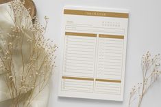 a white and gold printable planner next to some dried flowers on a white surface