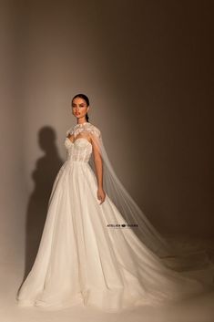 a woman in a white wedding dress with a veil on her head and shoulders, standing against a gray background