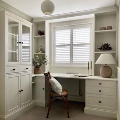 a chair sitting in front of a window next to a desk with a lamp on it