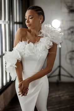 a woman in a white dress with feathers on her shoulder and one hand on her hip