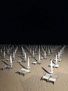 rows of beach chairs and umbrellas in the sand at night with lights on them