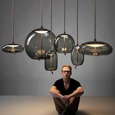 a man sitting on the floor in front of a chandelier with five lights hanging from it