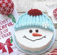 a snowman cake sitting on top of a wooden table next to christmas ornaments and decorations