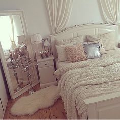 a white bed with pillows and blankets on top of it next to a mirror in a room