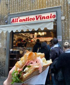 a person holding up a sandwich in front of a store