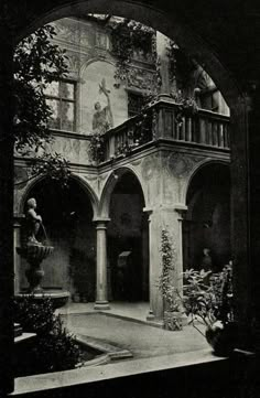 black and white photograph of an old building with statues on the balcony, surrounded by greenery