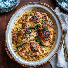 a bowl filled with chicken and gravy on top of a wooden table next to silverware