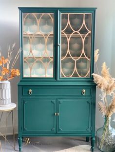 a green china cabinet sitting next to a vase with dried flowers in it on top of a rug