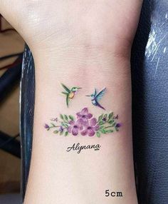 a small tattoo on the wrist with flowers and two hummings flying above it, which reads alunana