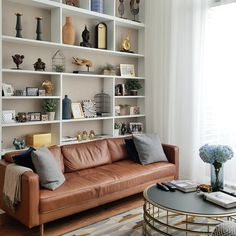 a brown leather couch sitting in front of a white book shelf filled with vases