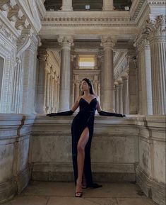 a woman in a long black dress standing on a ledge with her legs spread out