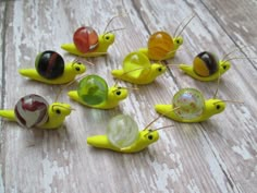 small yellow plastic snails sitting on top of a wooden table next to each other with different colored glass balls in them